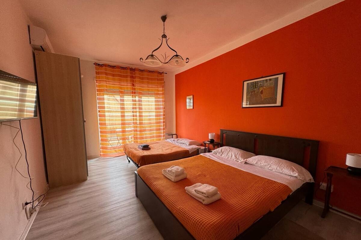 Een hotelkamer met twee bedden, een houten garderobe, een schilderij aan de muur en een raam met gestreepte gordijnen.