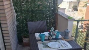 A small balcony with a table set for two, surrounded by greenery and a cityscape in the background. - Bibbi's House San Lorenzo (Rome)