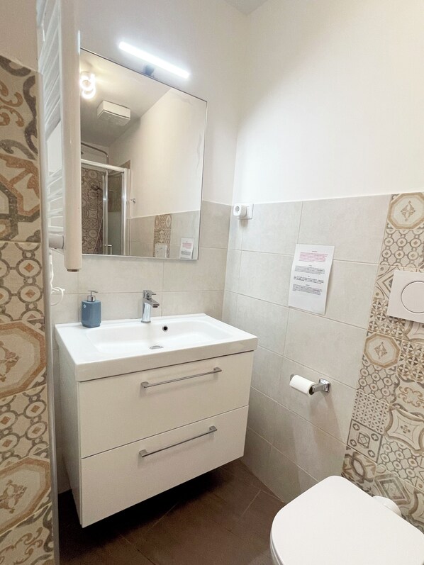 Un baño con lavamanos, espejo y retrete blanco.