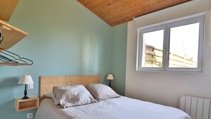 A bedroom with a bed, two bedside lamps, a wooden headboard, a window, and a radiator. - Apartment with private garden and modern amenities (Groix)