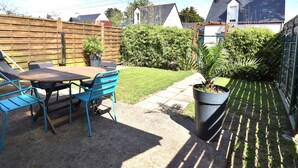 A patio with a table and chairs, a potted plant, and a garden area with a fence and greenery. - Apartment with private garden and modern amenities (Groix)