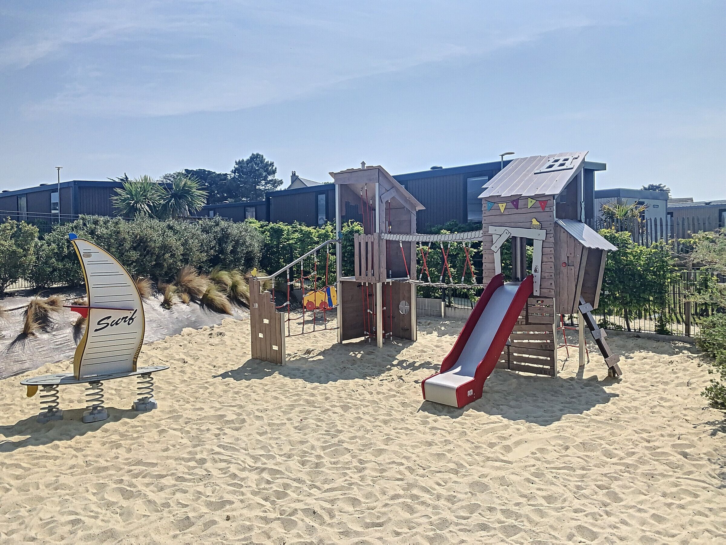 Una playa arenosa con una estructura de madera para juegos, que incluye un tobogán y columpios.