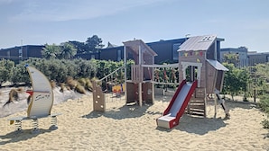 Une plage de sable avec une structure de jeux en bois, comprenant un toboggan et une balançoire.