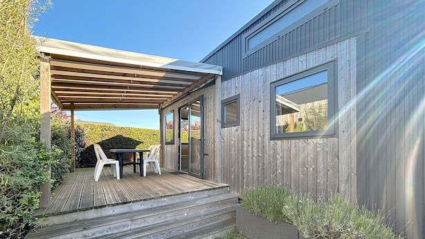Une maison moderne dotée d’une terrasse en bois, d’un patio couvert et d’un jardin.