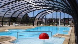 Une piscine intérieure dotée d’un toit en verre, de chaises longues et d’un élément décoratif aquatique rouge.
