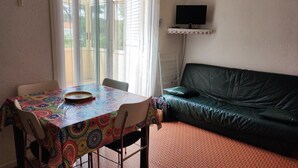 Ein Zimmer mit Esstisch, Stühlen, einer Couch und einem Fernseher an der Wand.