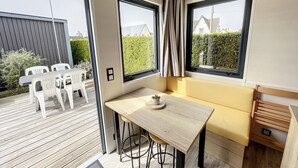 Eine moderne Küche mit Holztisch und Barhocker, großen Fenstern mit Vorhängen und Blick ins Freie.