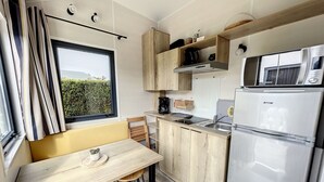 Eine kleine Küche mit Holztisch, Barhocker, Kühlschrank, Mikrowelle und einem Fenster mit Vorhängen.