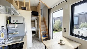 Eine kleine Küche mit integriertem Kühlschrank, einem Spülbecken und einer Holztreppe, die zu einem Schlafbereich führt.