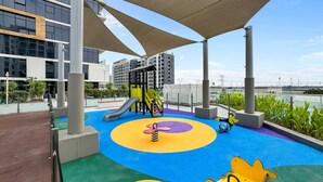 A playground with slides and swings, surrounded by a modern building. - Sleek Studio Apartment in Azizi Riviera- Suiteable (Dubai)