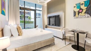 A modern hotel room with a large bed, a TV, a dining area, and a view of the city. - Sleek Studio Apartment in Azizi Riviera- Suiteable (Dubai)