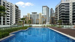 A swimming pool surrounded by modern buildings, with a clear sky above. - Sleek Studio Apartment in Azizi Riviera- Suiteable (Dubai)