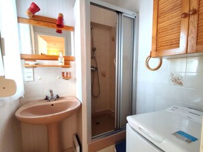 Features a compact bathroom with a sink, toilet, glass shower enclosure, and wooden cabinets.