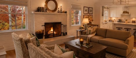 A cozy living room with a fireplace, patterned furniture, and a kitchen in the background.