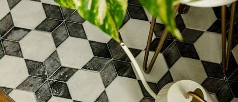 A bathroom with a black and white hexagonal tile floor, a white kettle, and a green potted plant.