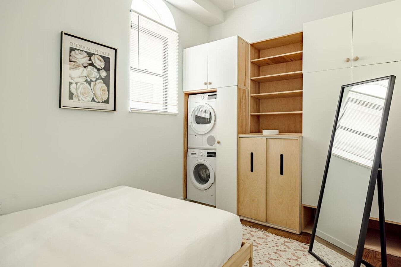 A bedroom with a bed, a washing machine, wooden cabinets, and a framed picture on the wall.