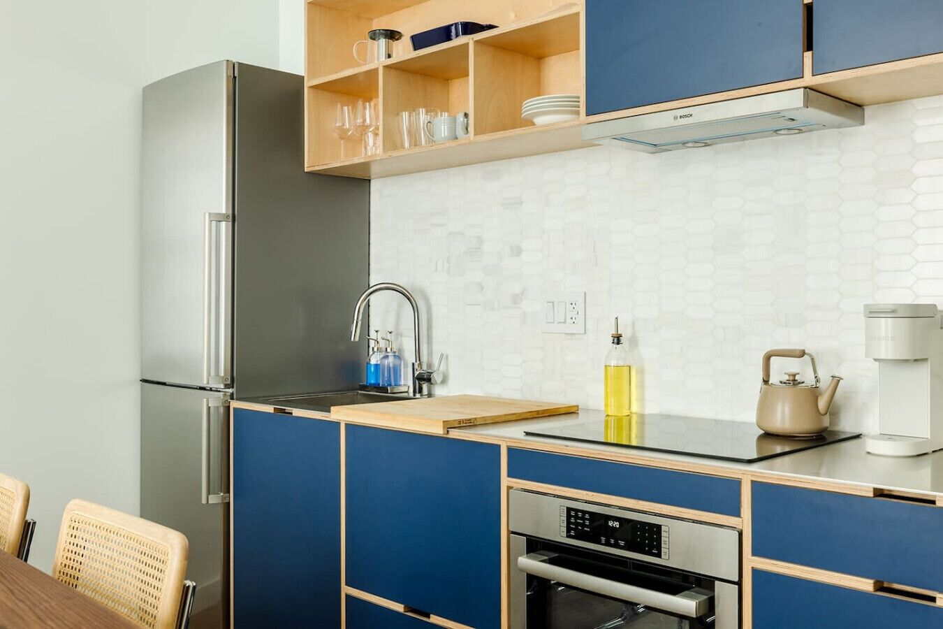 A modern kitchen with a stainless steel refrigerator, a built-in oven, a coffee maker, and a kettle on the counter.