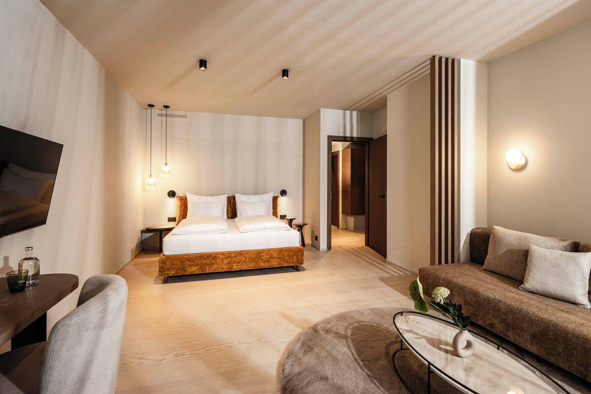 A modern hotel room with a large bed, a sofa, a TV, and a dining area.