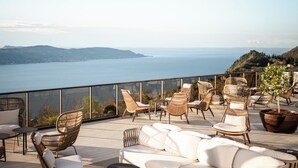 Una terraza con mobiliario de mimbre, una planta en maceta y vistas al mar y a las colinas.