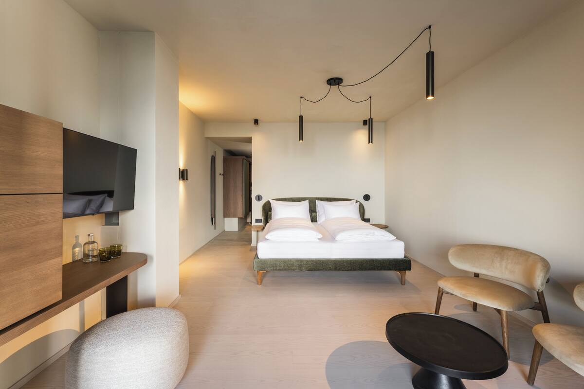 A modern hotel room with a bed, seating area, and a TV.