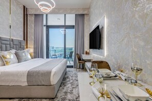 A modern hotel room with a large bed, a dining area, a TV mounted on the wall, and a view of the city through large windows. - GLOBALSTAY. Azizi Riviera 48 (Dubai)