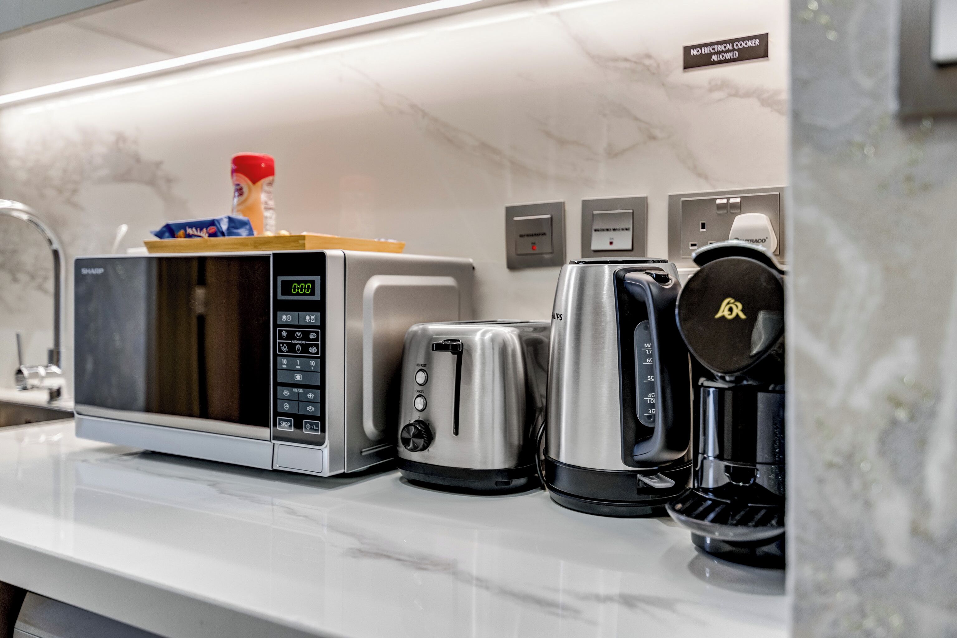 Een keuken met een magnetron, broodrooster en koffiezetapparaat op een marmeren aanrecht.