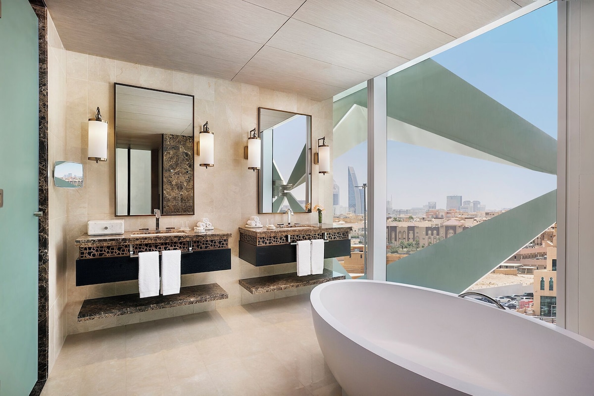 A modern bathroom with two sinks, large mirrors, and a freestanding bathtub.
