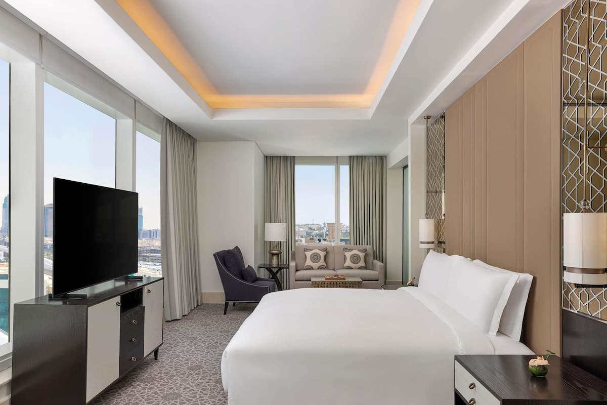 Ein Hotelzimmer mit einem großen Bett, einem Fernseher, einem Schreibtisch und einem Sessel.