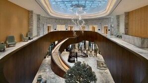 A modern hotel lobby with a central spiral staircase, marble flooring, and a skylight ceiling.