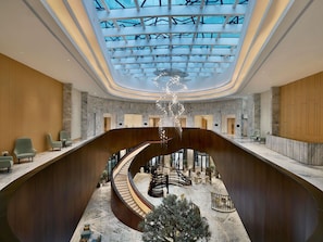 A modern hotel lobby with a central spiral staircase, marble flooring, and a skylight ceiling.