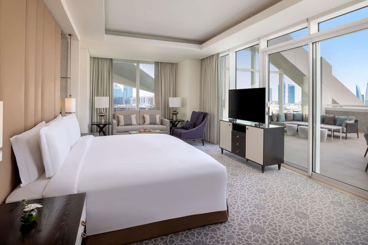 A hotel room with a large bed, a flat-screen TV, a sofa, a desk, and a city view.