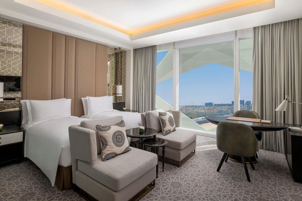 Habitación de hotel con una cama grande, dos sofás, una mesita y vistas a la ciudad.