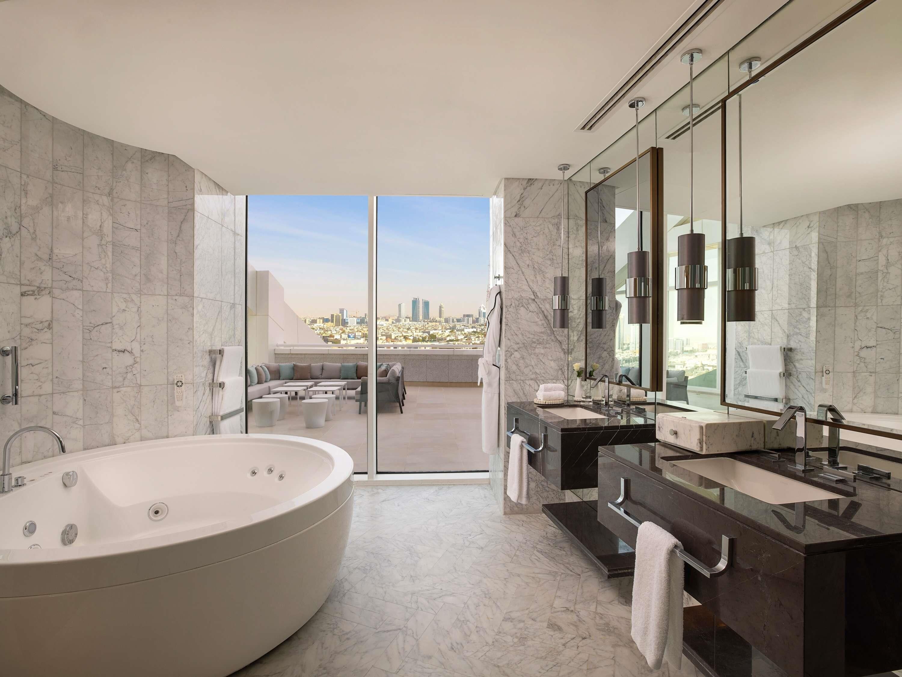 Un baño moderno con una bañera grande, un tocador con espejo y una zona de estar con vistas a la ciudad.