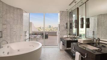 Un baño moderno con una bañera grande, un tocador con espejo y una zona de estar con vistas a la ciudad.