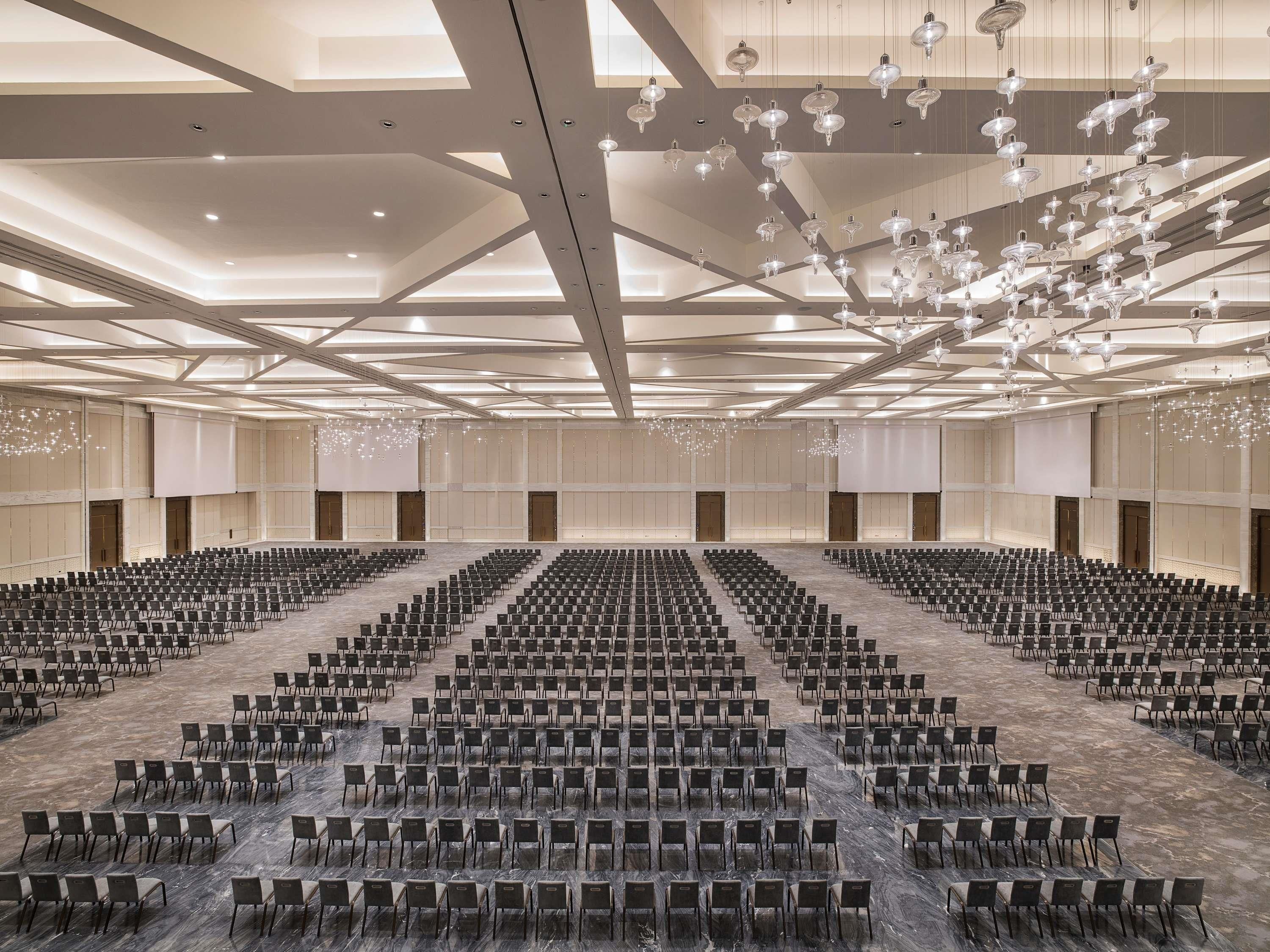 A large conference room with rows of chairs, a high ceiling with hanging lights, and a marble floor.