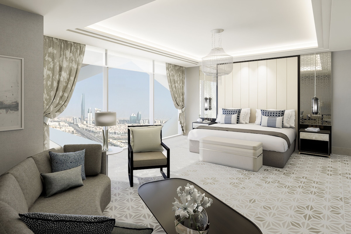 A modern hotel room with a city view, a bed, a sofa, a coffee table, and a desk.