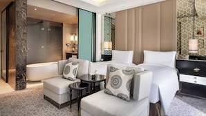 A hotel room with a large bed, two armchairs, a small table, a bathtub, and a vanity with a mirror.