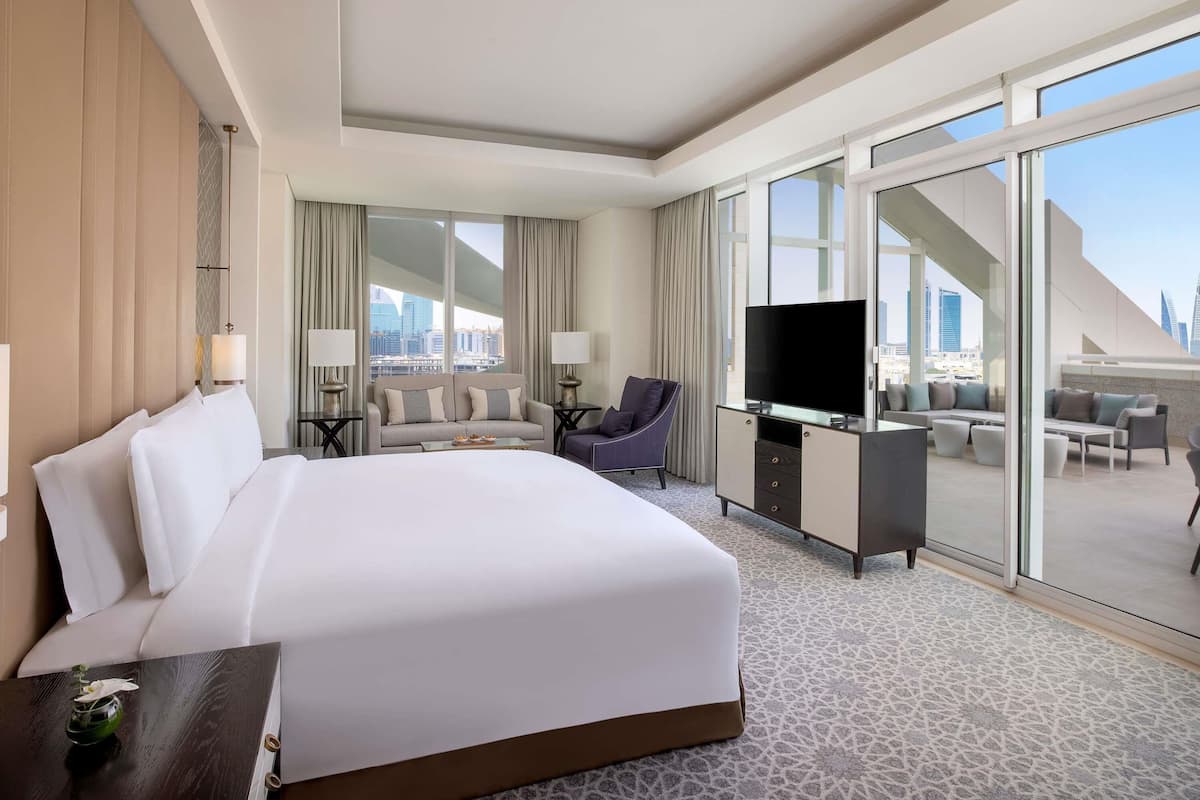Ein Hotelzimmer mit einem großen Bett, einem Schreibtisch mit Fernseher, einer Couch und einem Balkon mit Blick auf die Stadt.