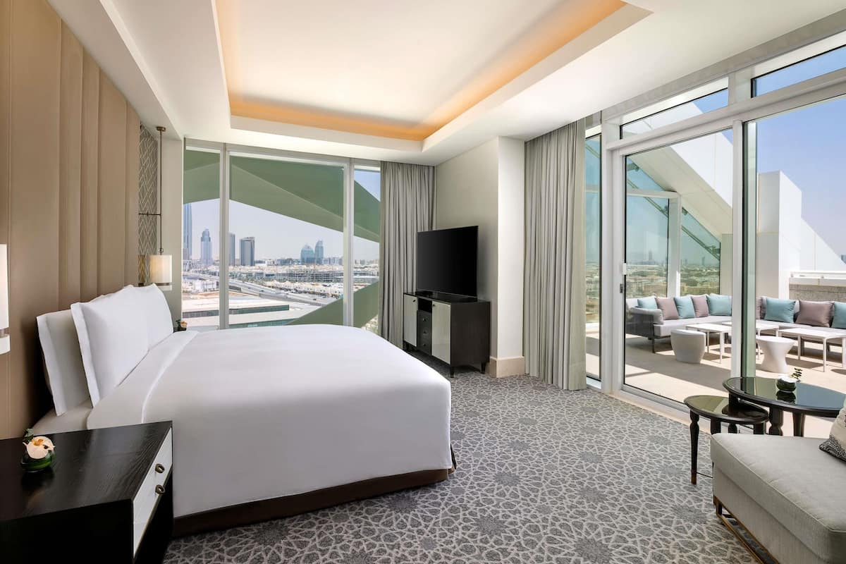 Ein Hotelzimmer mit einem großen Bett, einem Fernseher, einem Balkon mit Sitzgelegenheit und Blick auf die Stadt.