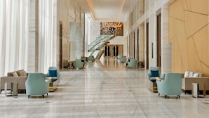 A spacious lobby with a central staircase, marble floors, and modern seating arrangements.