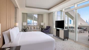 A hotel room with a large bed, a desk with a TV, a sofa, and a balcony with a city view.