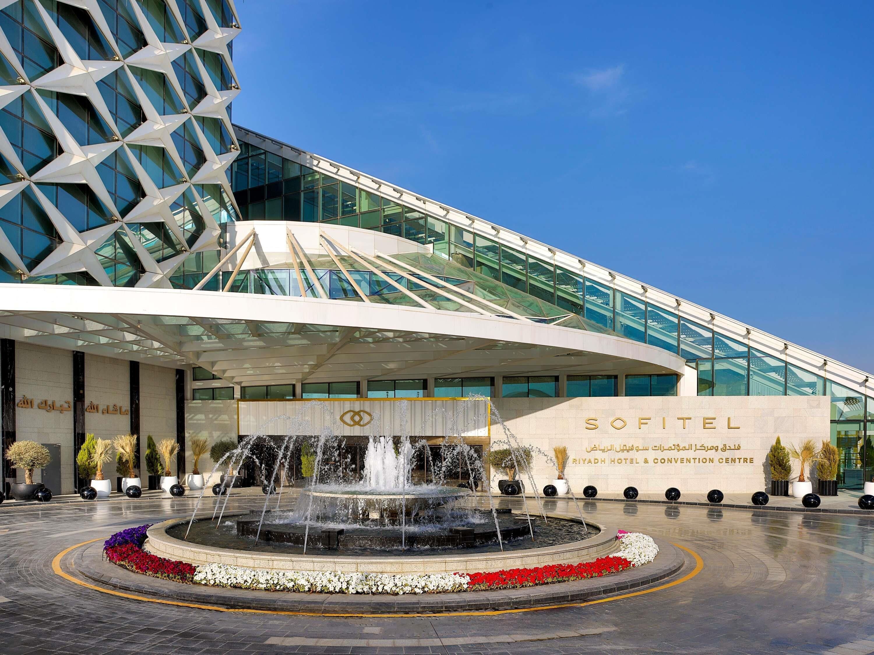A hotel entrance with a fountain, modern architecture, and a clear sky.