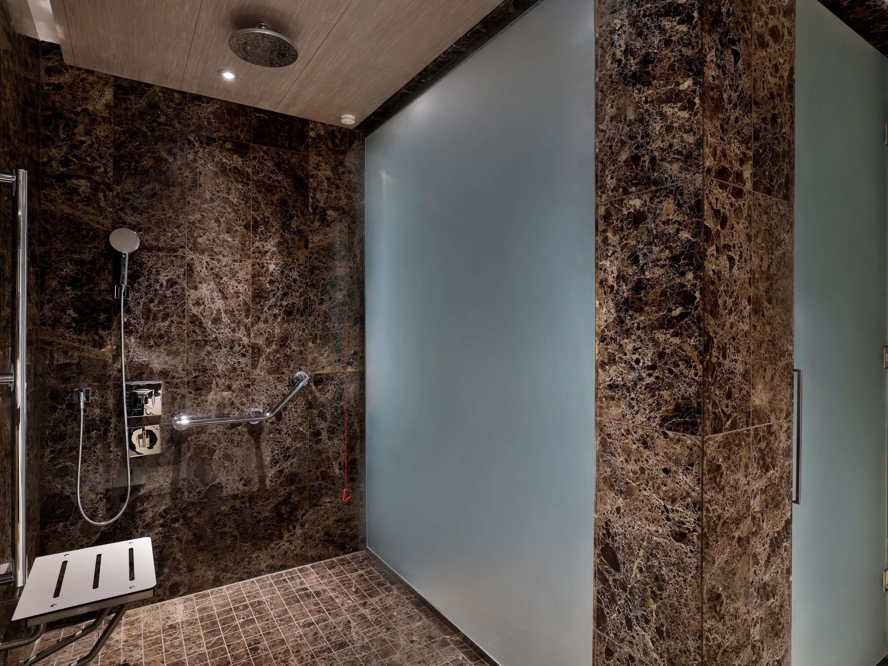 A modern bathroom with a shower, marble walls, and a glass partition.