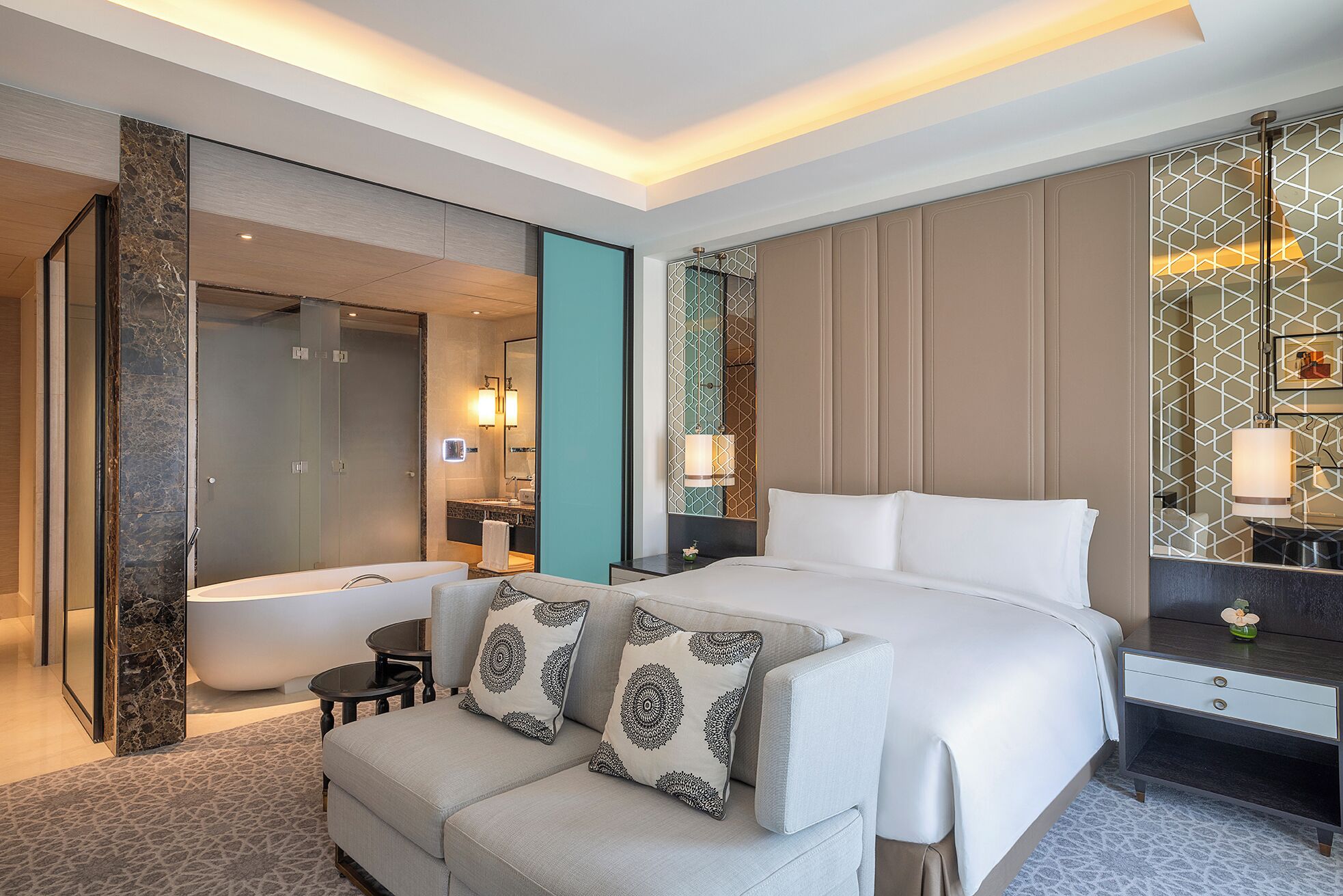 A modern hotel room with a large bed, a sitting area, a bathtub, and a bathroom with a glass shower enclosure.