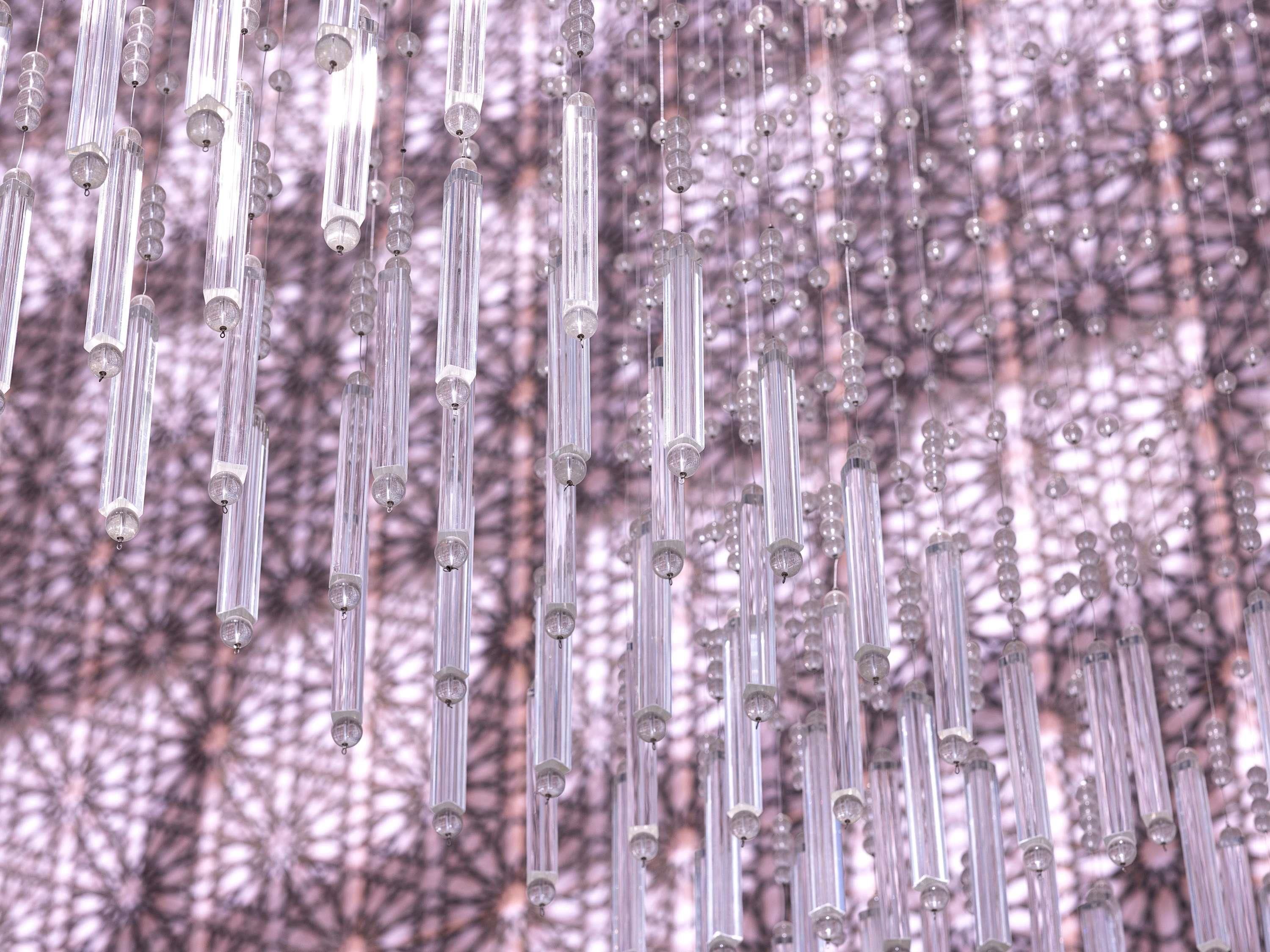 A series of vertical hanging structures with clear tubes and spherical elements, set against a patterned background.