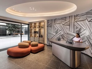 A reception area with a modern design, featuring a check-in counter, a seating area with orange ottomans, a patterned wall, and a glass door leading outside. - Tribe Auckland (Auckland)