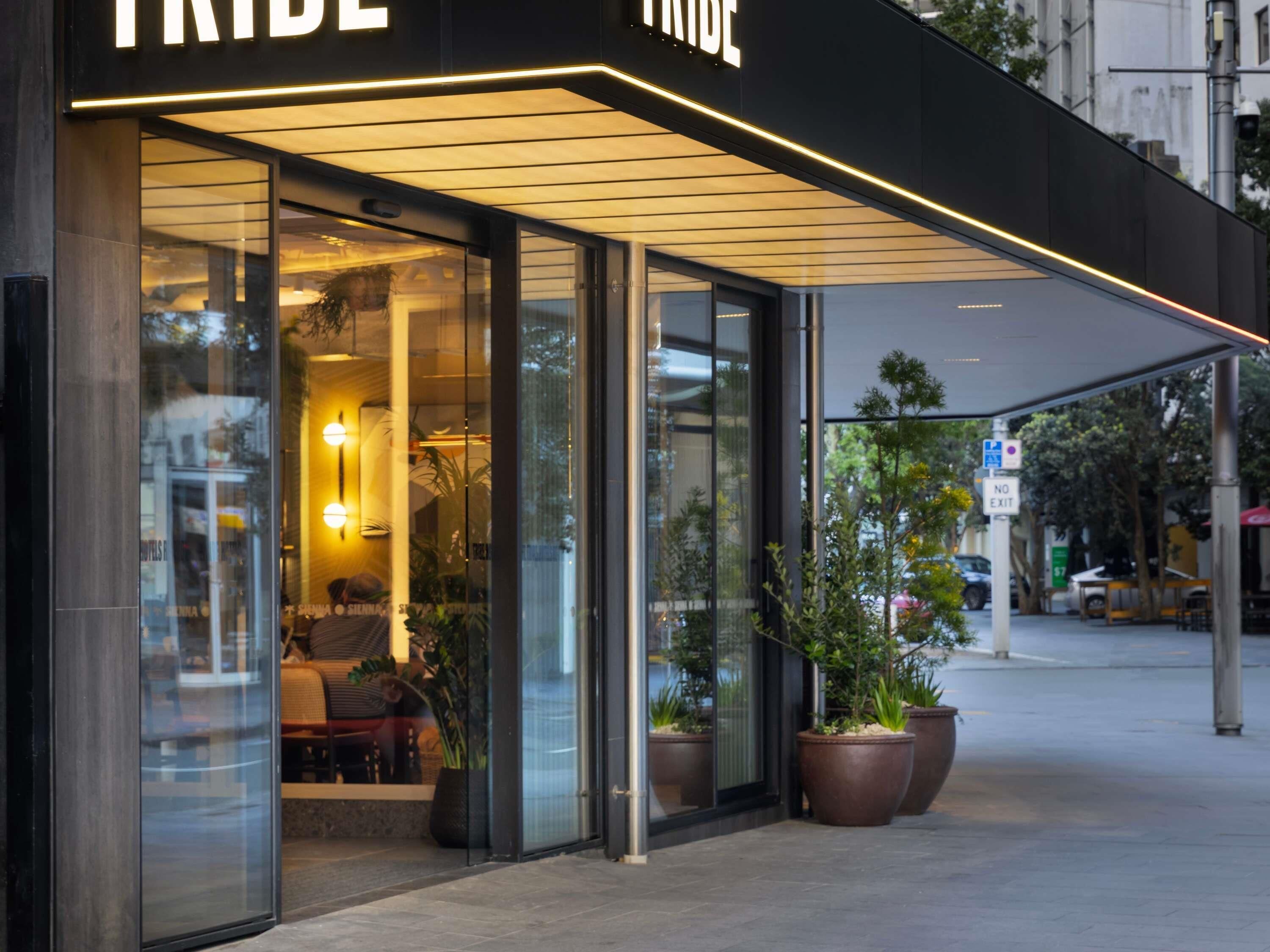 A hotel entrance with a glass facade, outdoor seating, and potted plants.