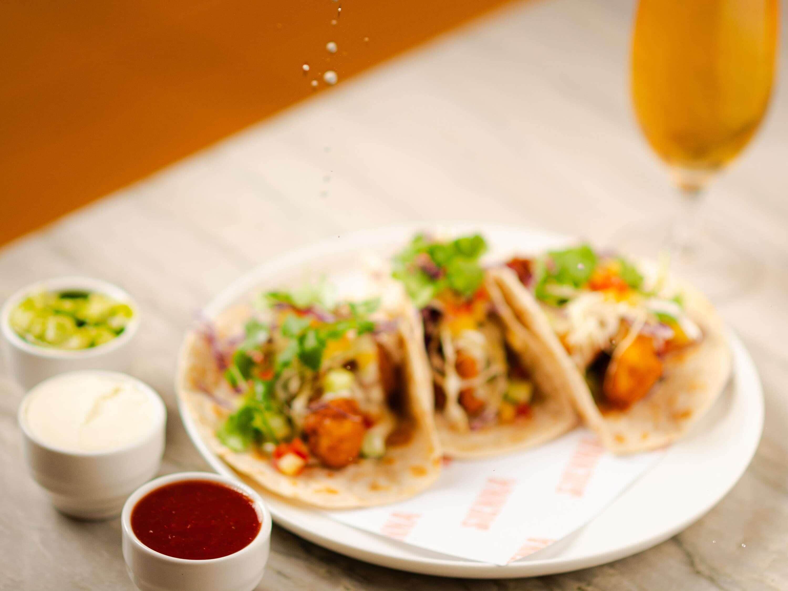 A plate of tacos with condiments and a glass of wine on a table.