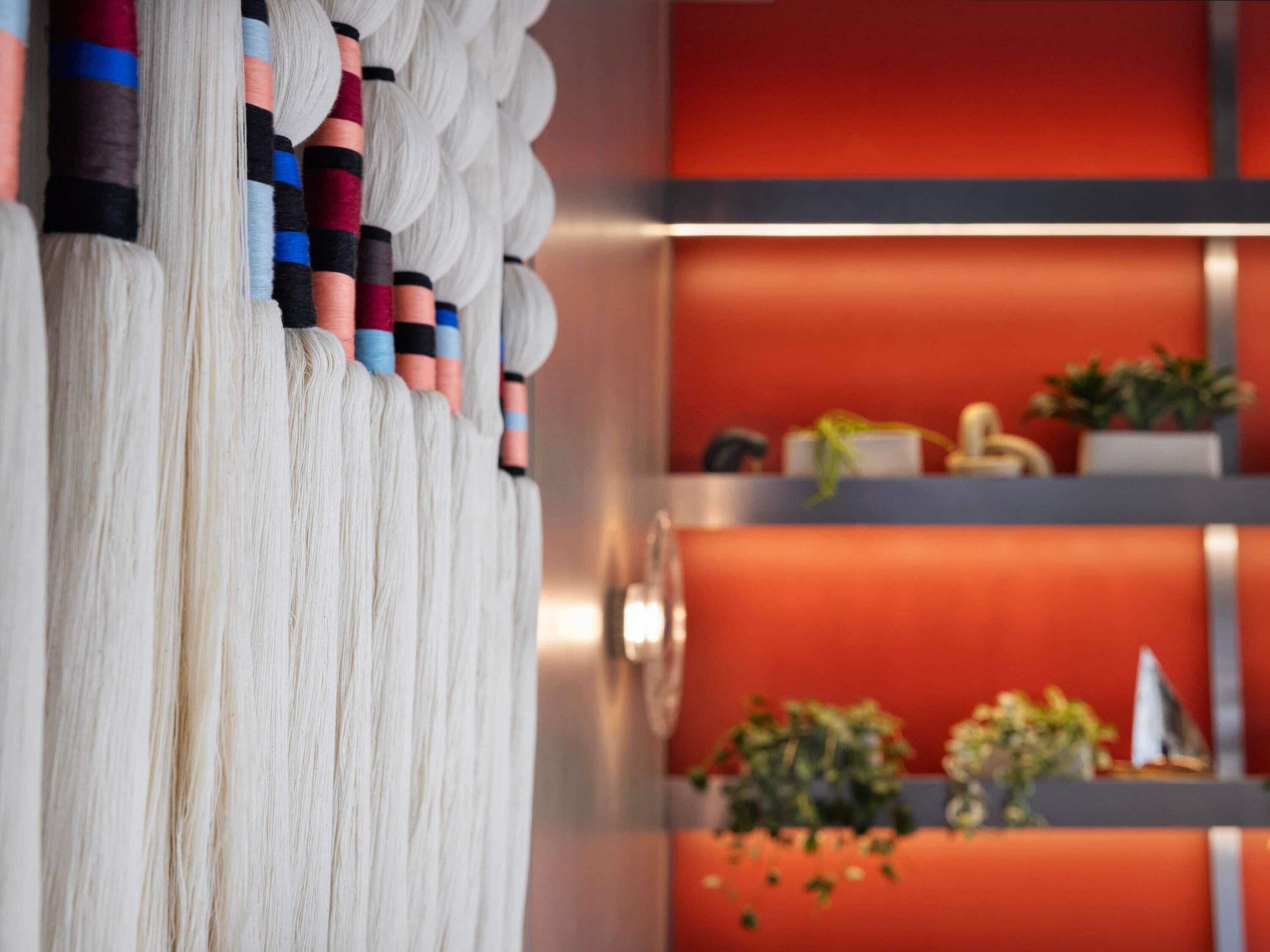 A room with a white curtain, a red wall, and a shelf with plants and a small decorative item.