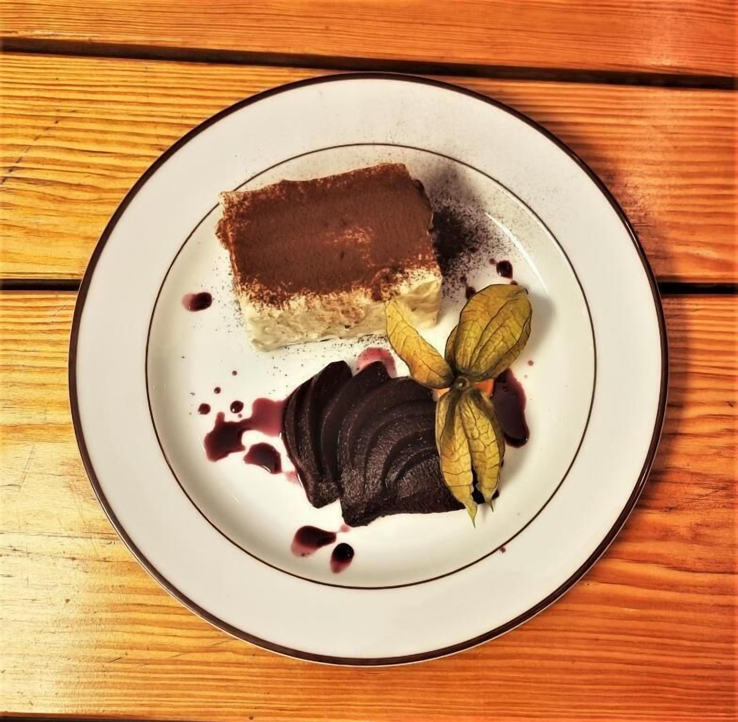 Un piatto dessert con una fetta di torta, un'assortimento di frutta e una cucchiaiata di panna su un tavolo di legno.